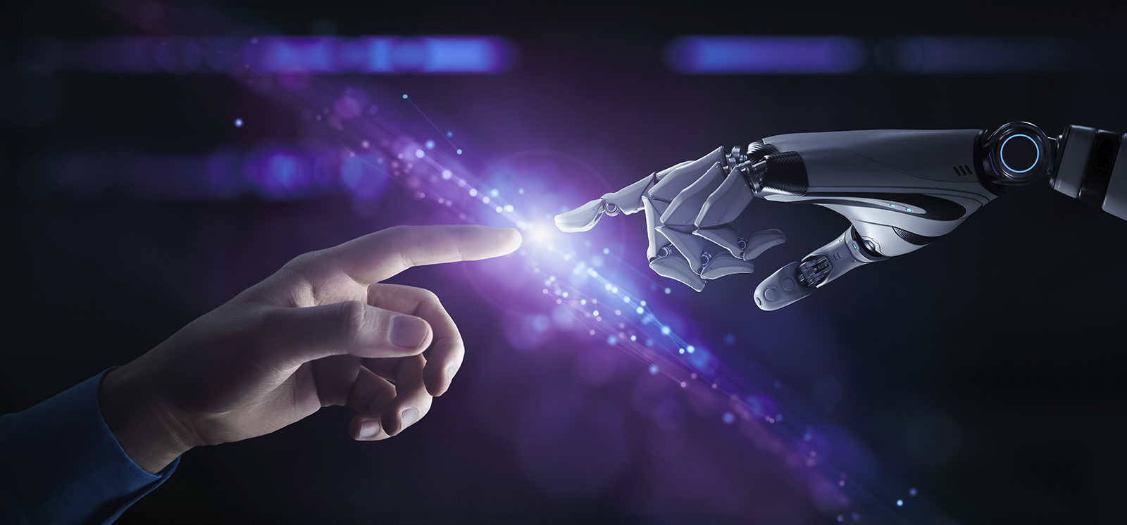 Symboliczny obraz ukazujący zbliżające się do siebie palce człowieka i robota na tle fioletowego światła, przedstawiający połączenie technologii i człowieczeństwa, współpracę człowieka z sztuczną inteligencją.